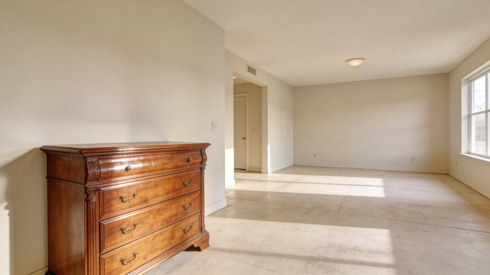 A classic wooden dresser stands against a plain white wall in a bright, spacious, and minimalist room.
